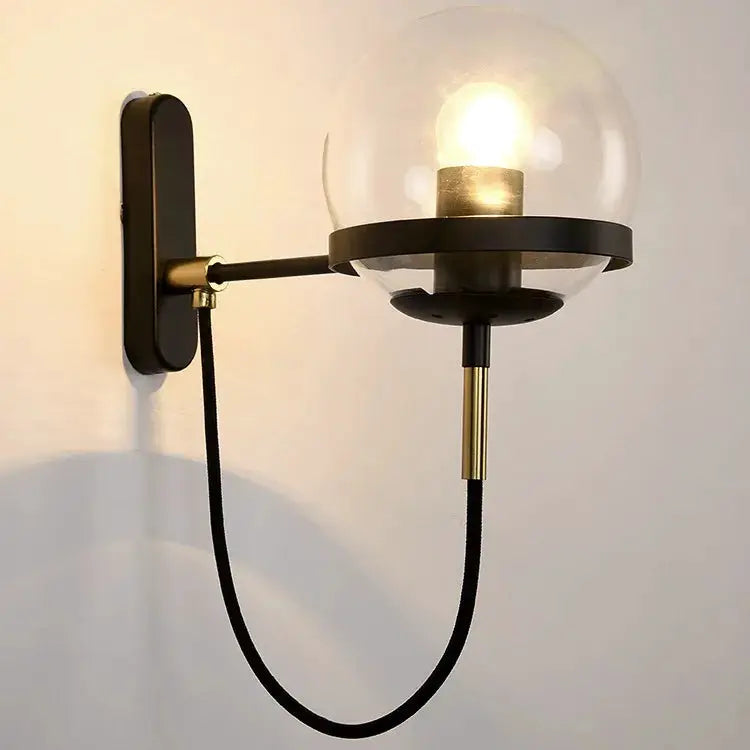 Modern glass ball wall lamp by Simples Market, black metal arm with clear globe shade and brass accents, E27