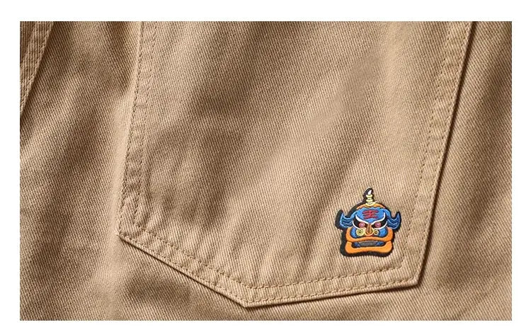 Beige cargo pants by Simples Market with an embroidered blue demon patch, straight-leg style.