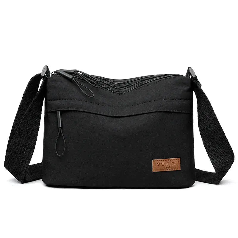 Crossbody bag, black canvas with three pockets and adjustable strap.