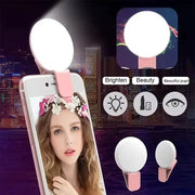 Portable LED selfie light clip for smartphones by Simples Market, pink base with white circular lamp, adjustable brightness.