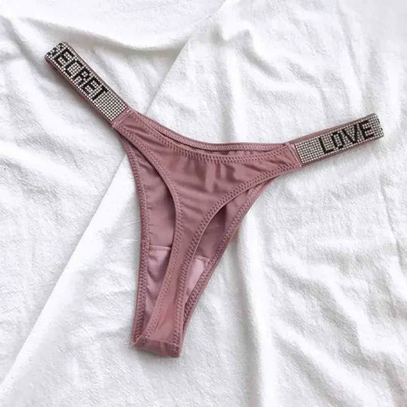 Pink low-rise thong with rhinestone letter waistband by Simples Market.