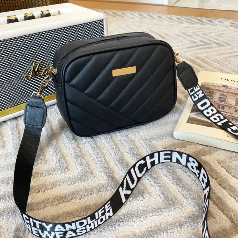 Shoulder bag black PU leather with diagonal quilted pattern, gold plaque accent, adjustable crossbody strap.