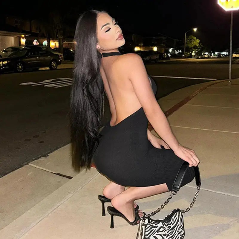 Hugcitar ribbed halter backless black bodycon jumpsuit worn by a woman with a zebra-print handbag and black heels