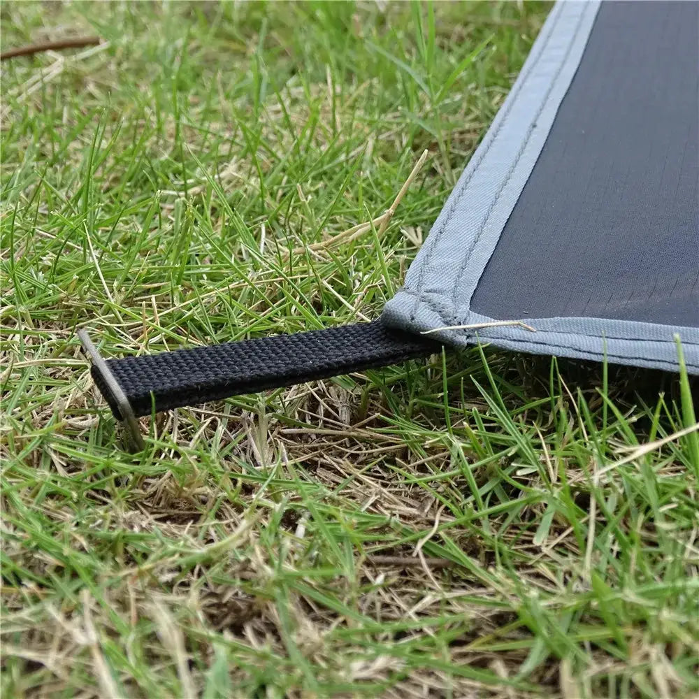 Waterproof camping mat with black carry strap and gray edge on grass