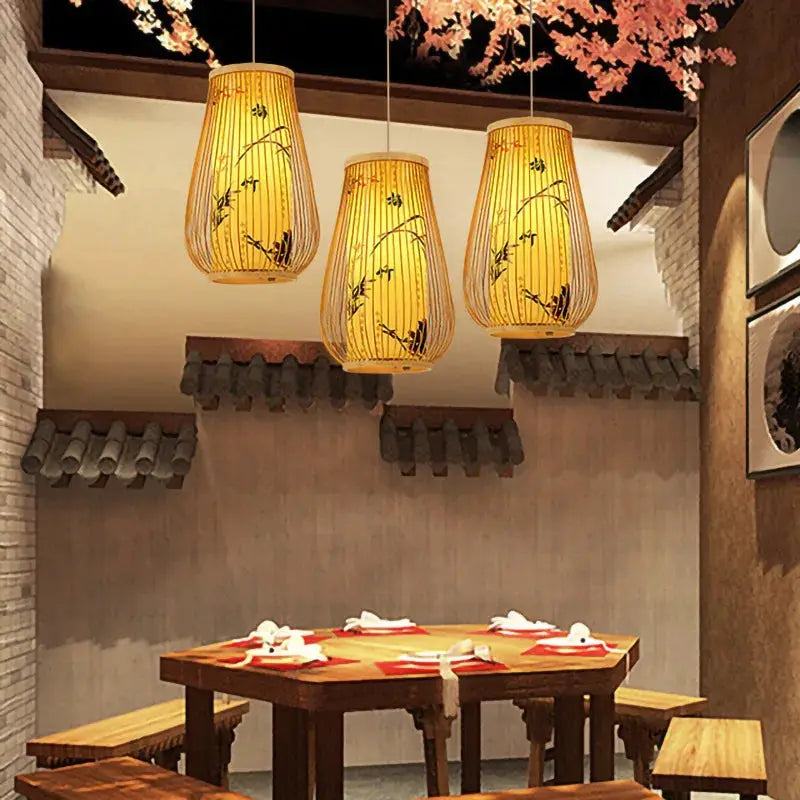 Three bamboo lantern chandeliers with warm amber glow over a wooden teahouse dining table.