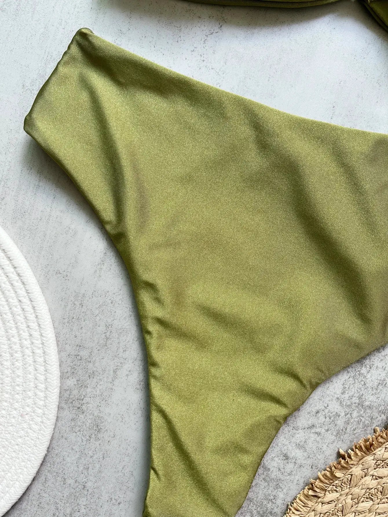 Bandeau bikini top in olive green satin fabric, solid beachwear on a textured surface.