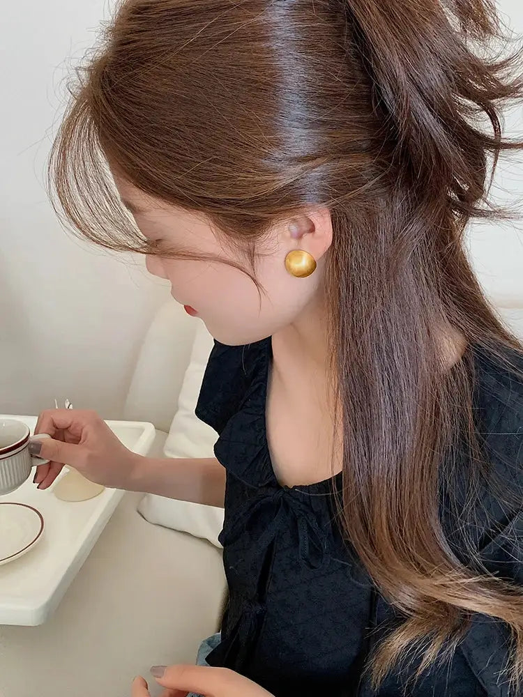 Earrings: gold-tone brushed metal round studs worn by a woman in a black top.