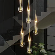 Five crystal LED teardrop pendant lights with gold-tone finishes hanging in a dark modern interior above a staircase