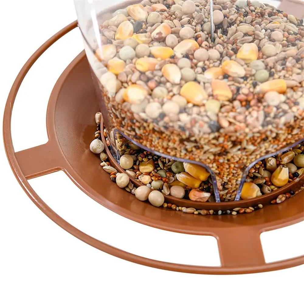Bird feeder with clear seed hopper and brown circular base, hanging multi-hole nut-and-seed dispenser.