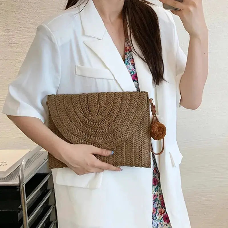 Handmade straw clutch bag with circular woven pattern in brown and a pom-pom charm
