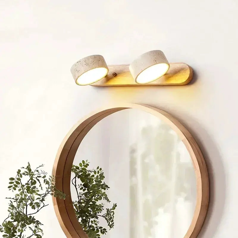 Two concrete-style LED wall lights on a wooden backplate above a round wooden-framed mirror.