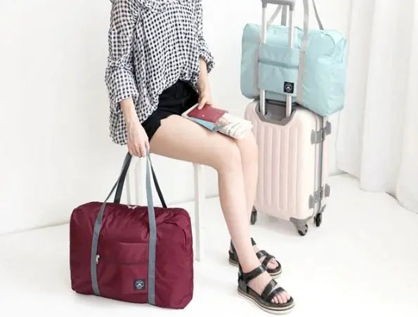 Simples Market large-capacity travel bag in burgundy with gray handles beside light-blue wheeled carry-on luggage