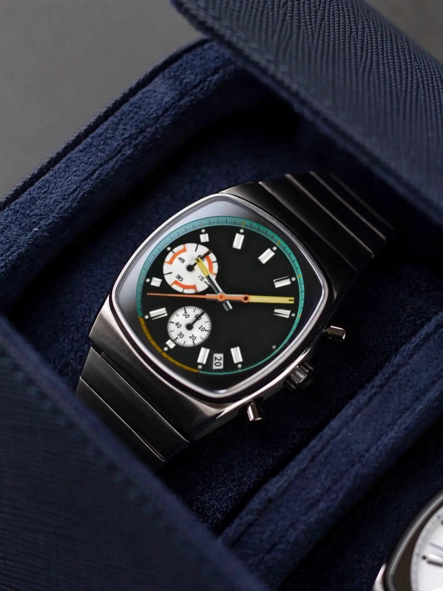 Men's vintage stainless steel wristwatch with black dial, colorful subdials and teal ring in a blue display case