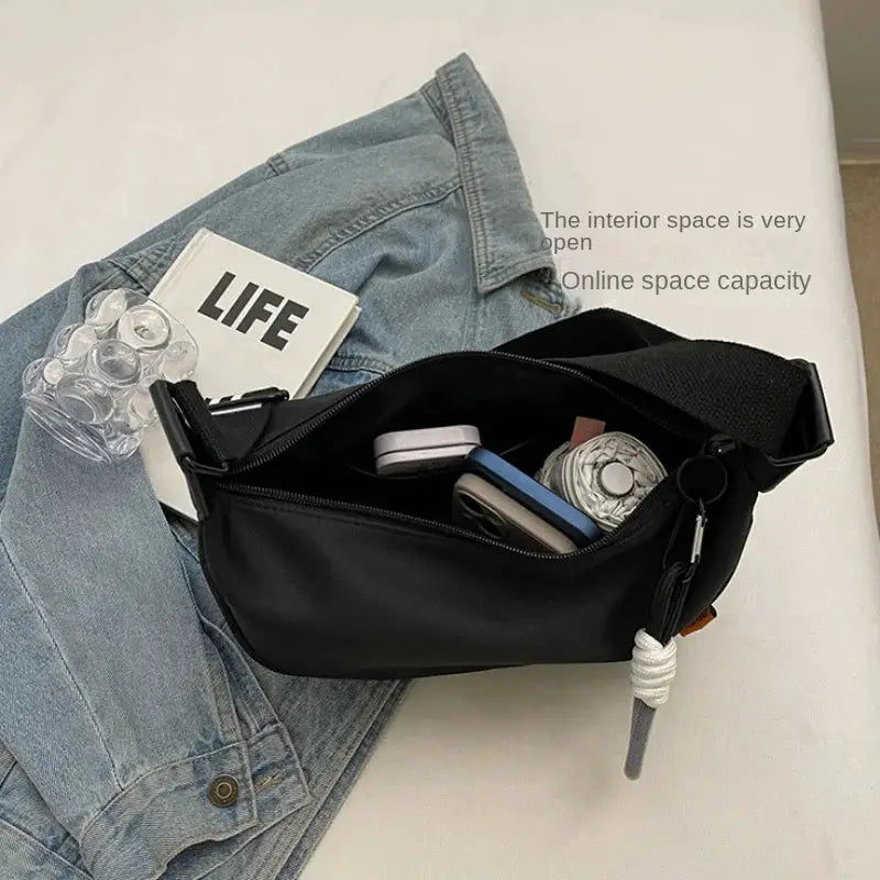 Simples Market black crossbody bag with a wide strap, open to reveal a phone and small items on a denim jacket.