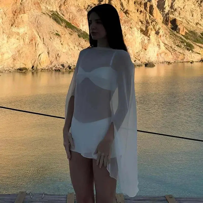 Chiffon see-through white cover-up cape worn over swimwear by a model at the seaside