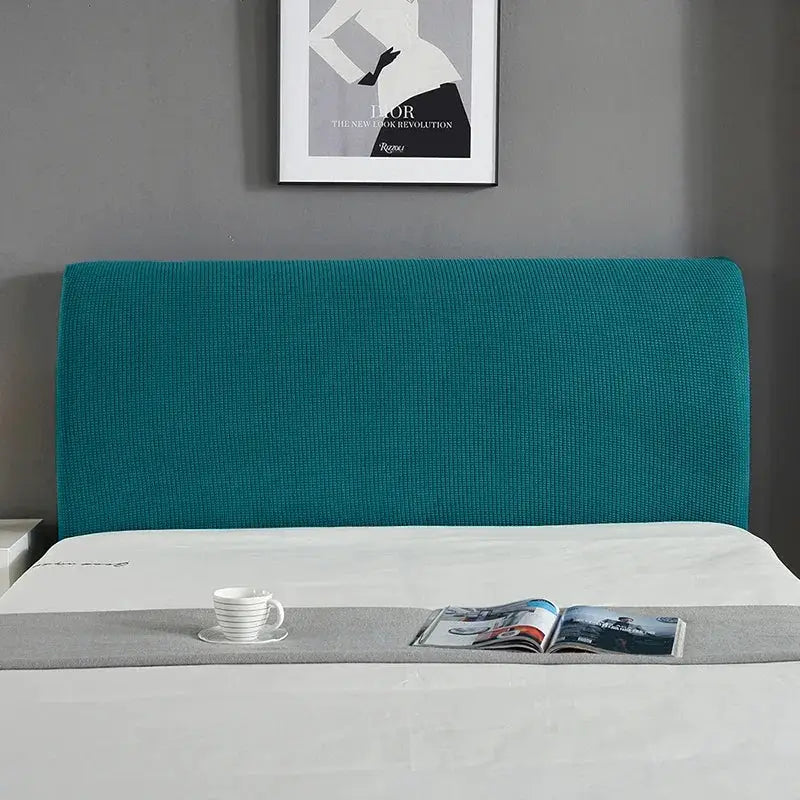 Bed headboard cover; teal padded headboard with white sheets, gray runner, cup and magazine.