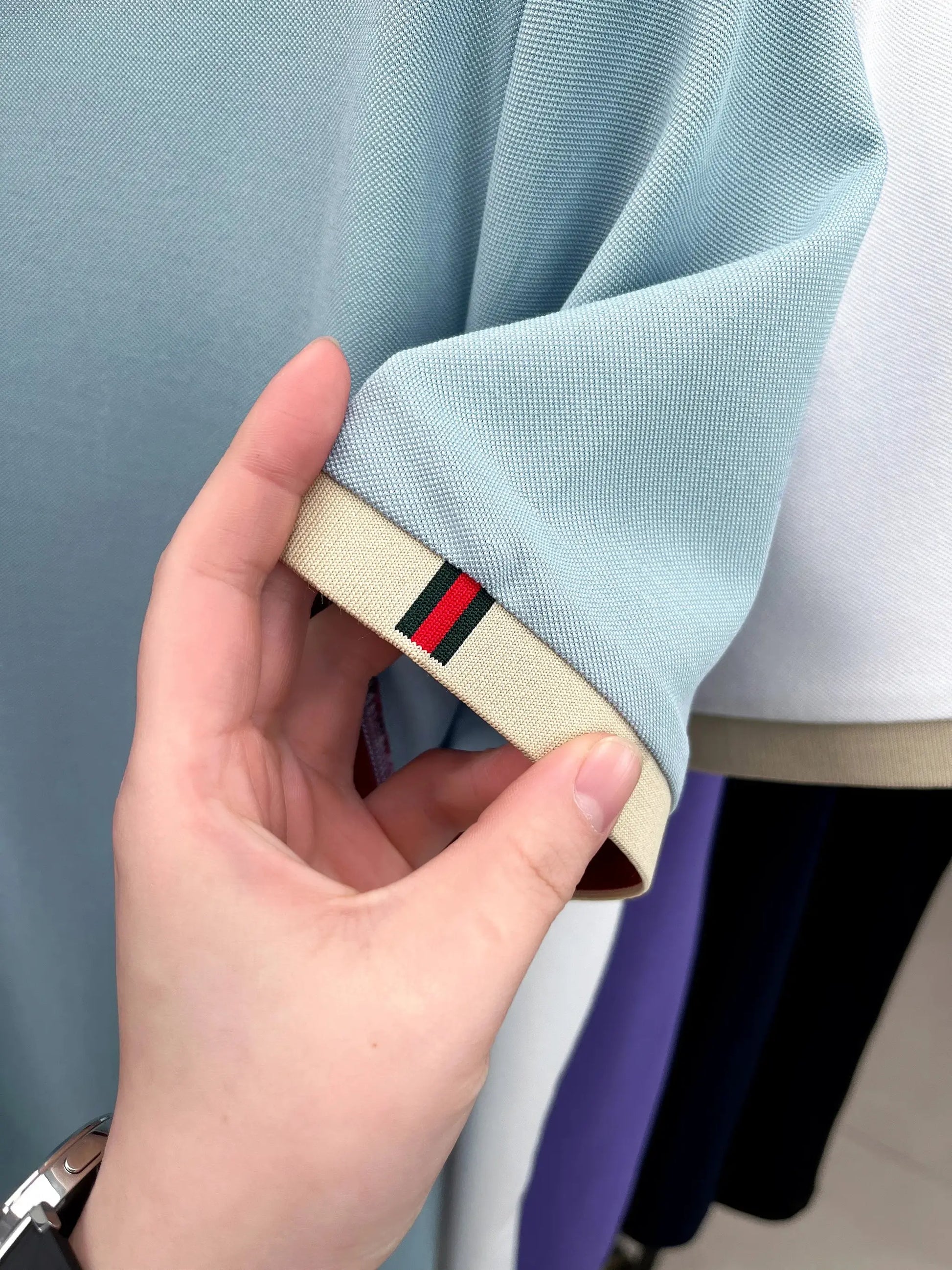 Light blue polo shirt sleeve with beige cuff trim and green-red striped detail