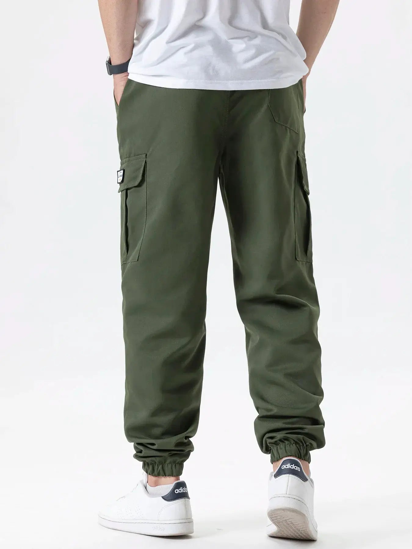 Men's olive green cargo joggers with multiple pockets, drawstring waist and elastic cuffs, paired with Adidas sneakers.