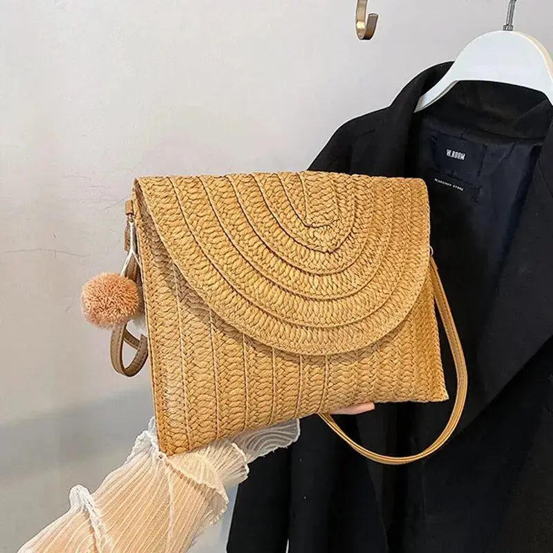 Straw beach crossbody bag by Simples Market, envelope-style woven clutch in natural beige with pom-pom charm