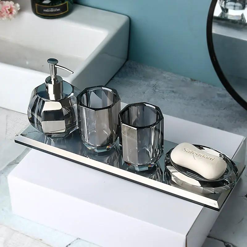 Four-piece glass bathroom set by Simples Market on a mirrored tray: crystal pump dispenser, two tumblers, and soap dish.