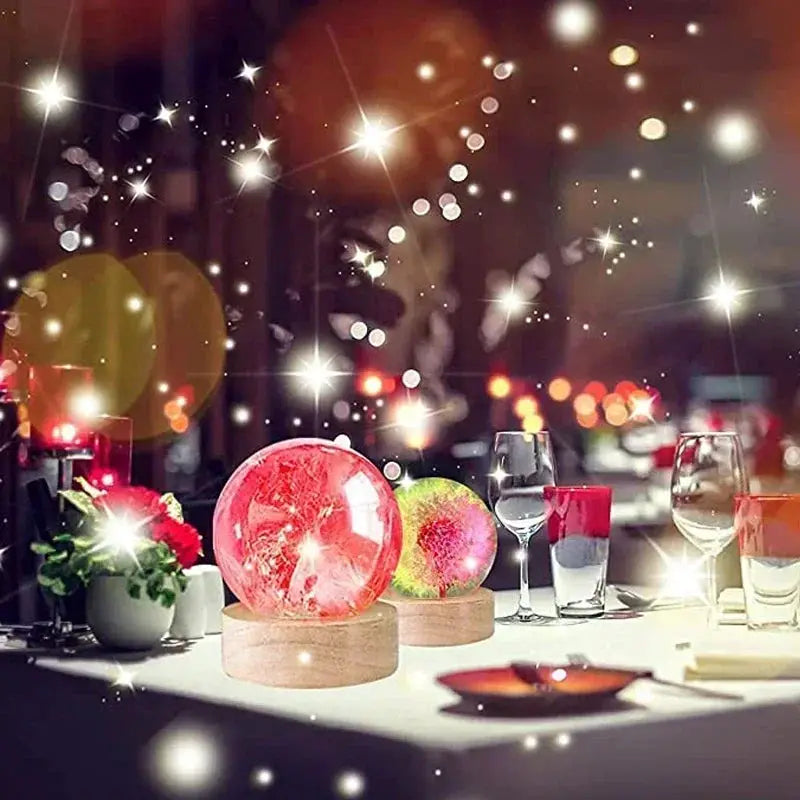 Two round wooden LED night light bases with 3D crystal glass balls in pink and multicolor, displayed on a dining table