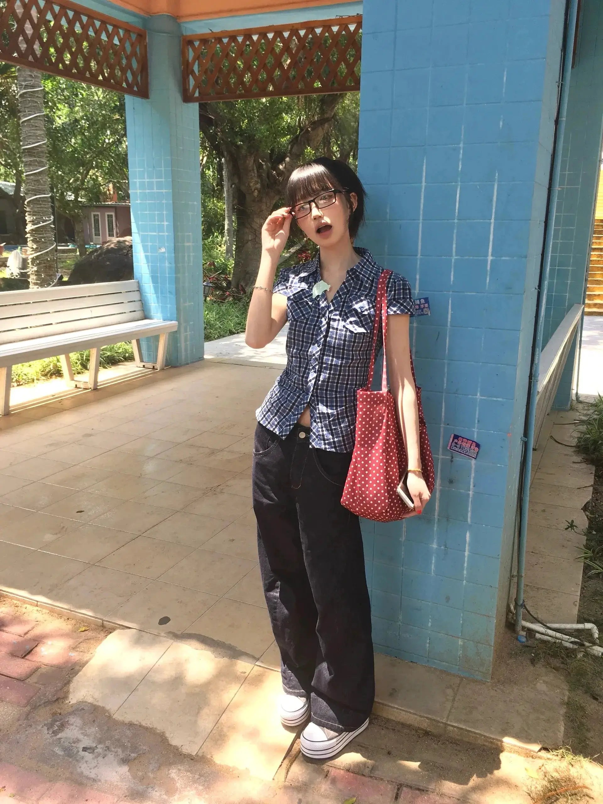 Karrram blue plaid short-sleeve shirt with V-neck worn by a woman beside a blue wall, carrying a red polka-dot bag.