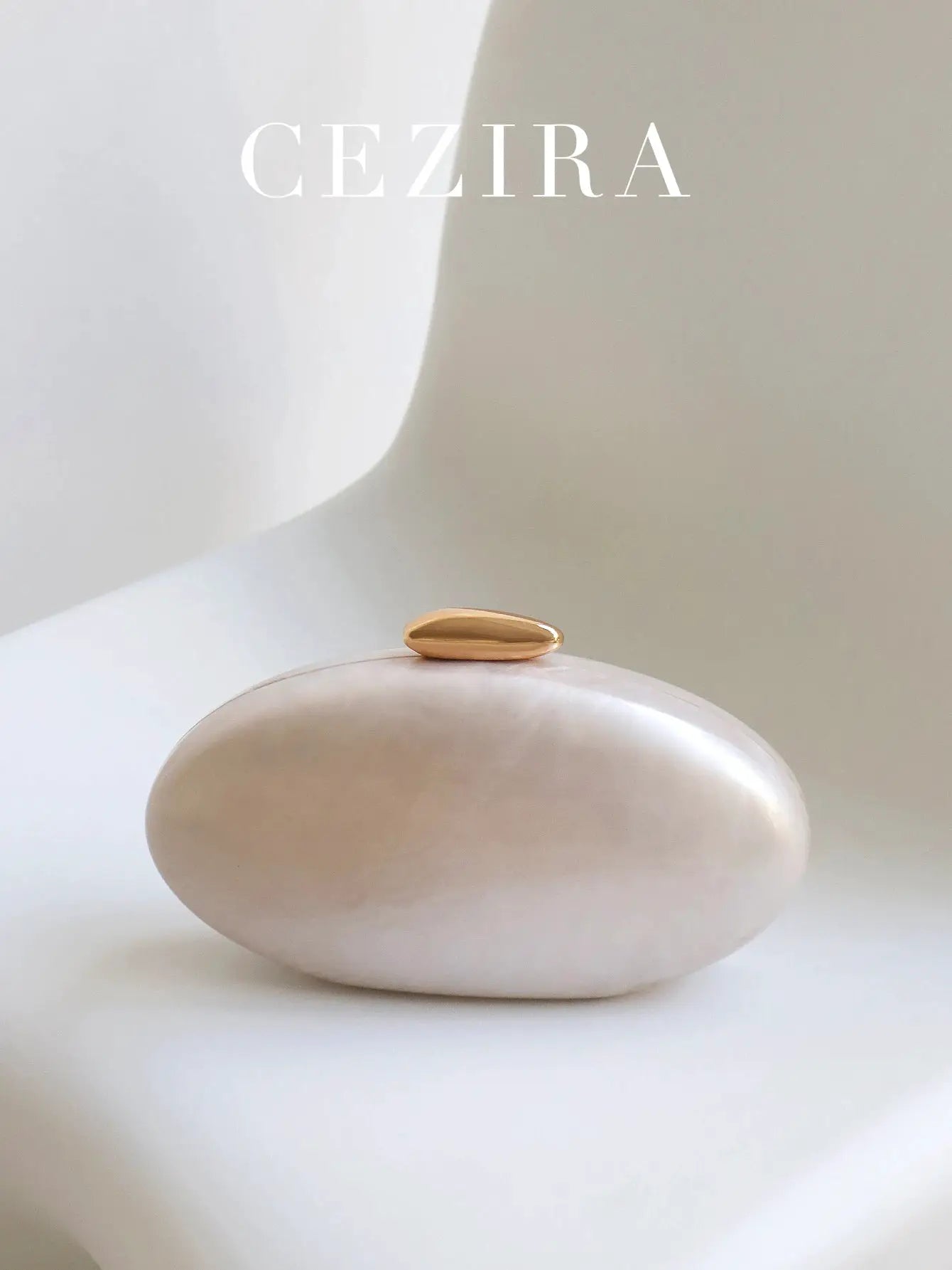 Oval gold clutch by CEZIRA on a white rounded stone backdrop