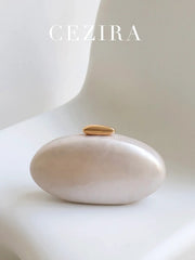 Oval gold clutch by CEZIRA on a white rounded stone backdrop