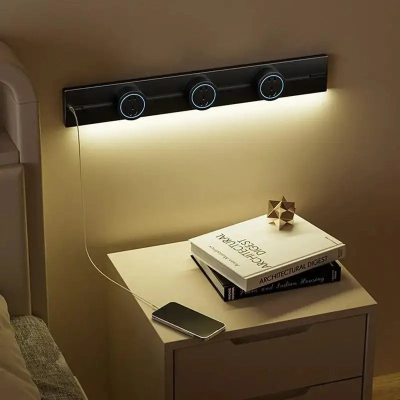 Black wall-mounted three-outlet track rail with blue-lit circular sockets above a bedside table