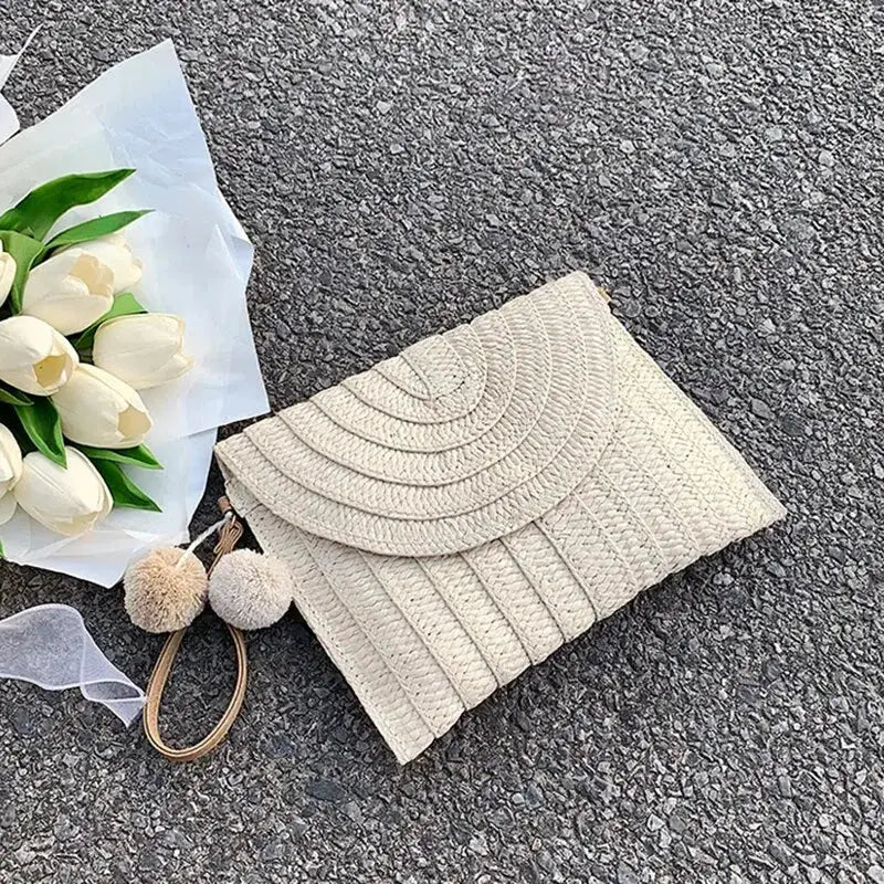 Handmade straw beach crossbody bag by Simples Market, beige woven with envelope flap and pom-pom keychain.