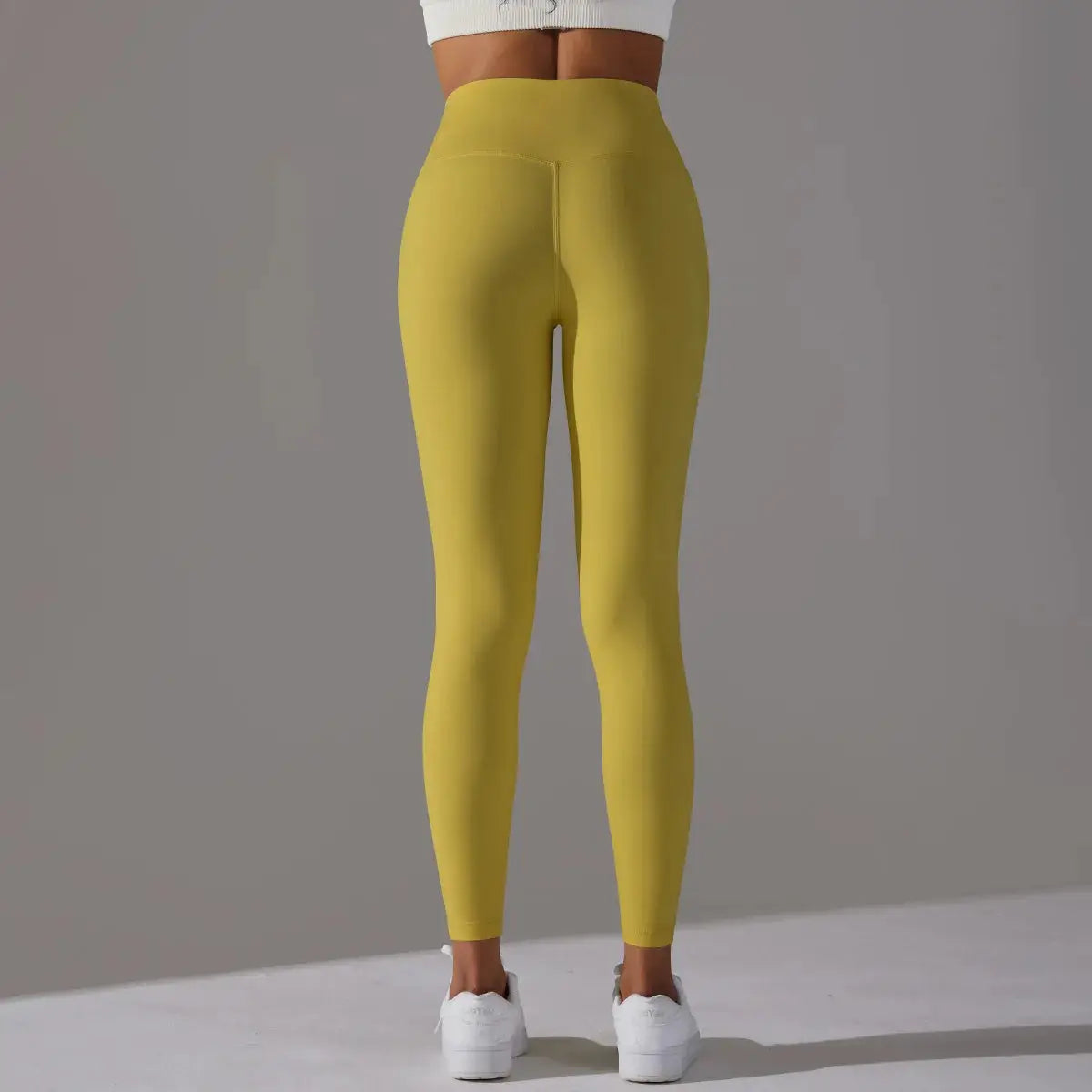 Women’s high-waist naked-feeling leggings in mustard yellow; back view, ideal for fitness, running and yoga, tight fit.