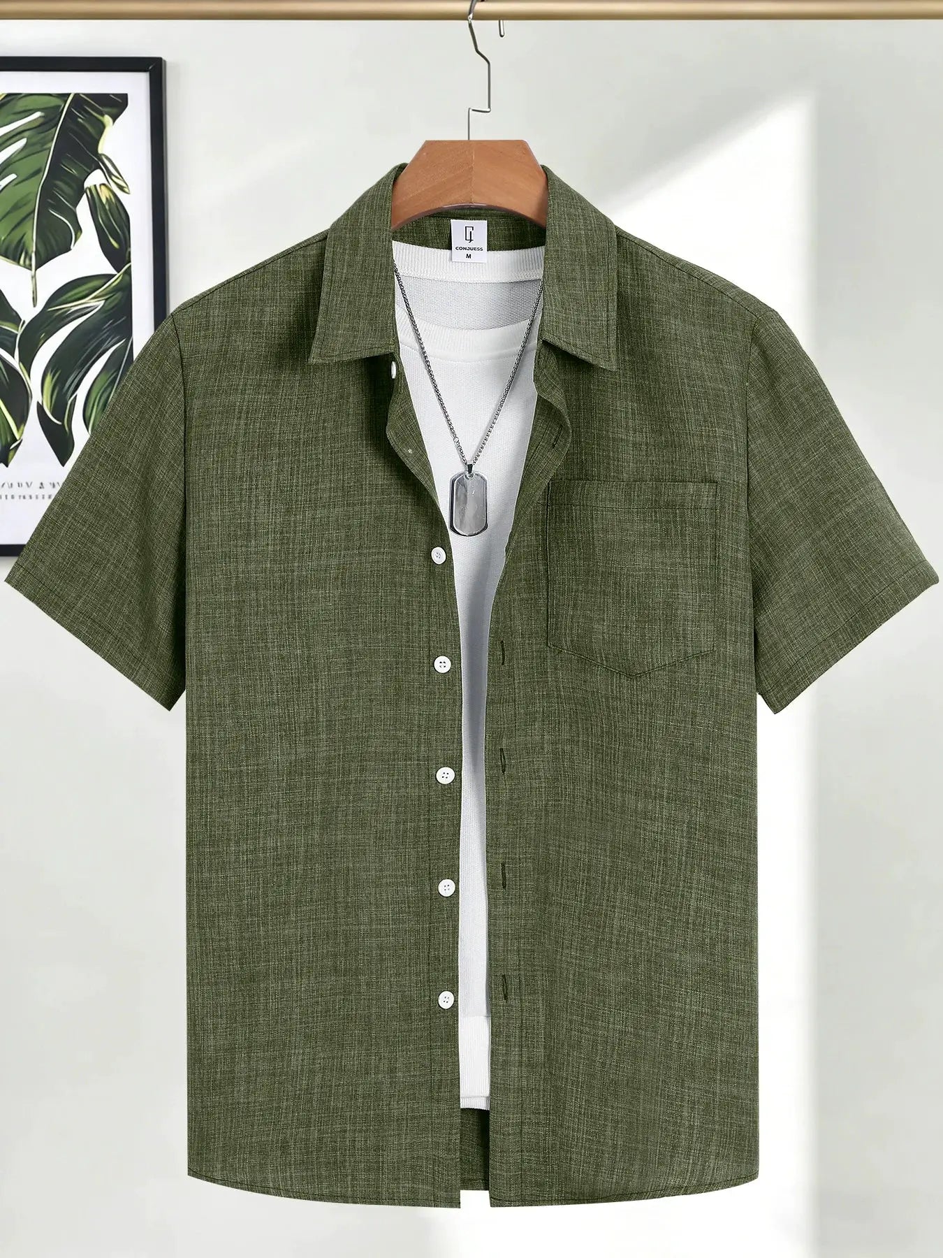 Men's olive-green linen short-sleeve shirt on hanger over white tee with dog-tag necklace