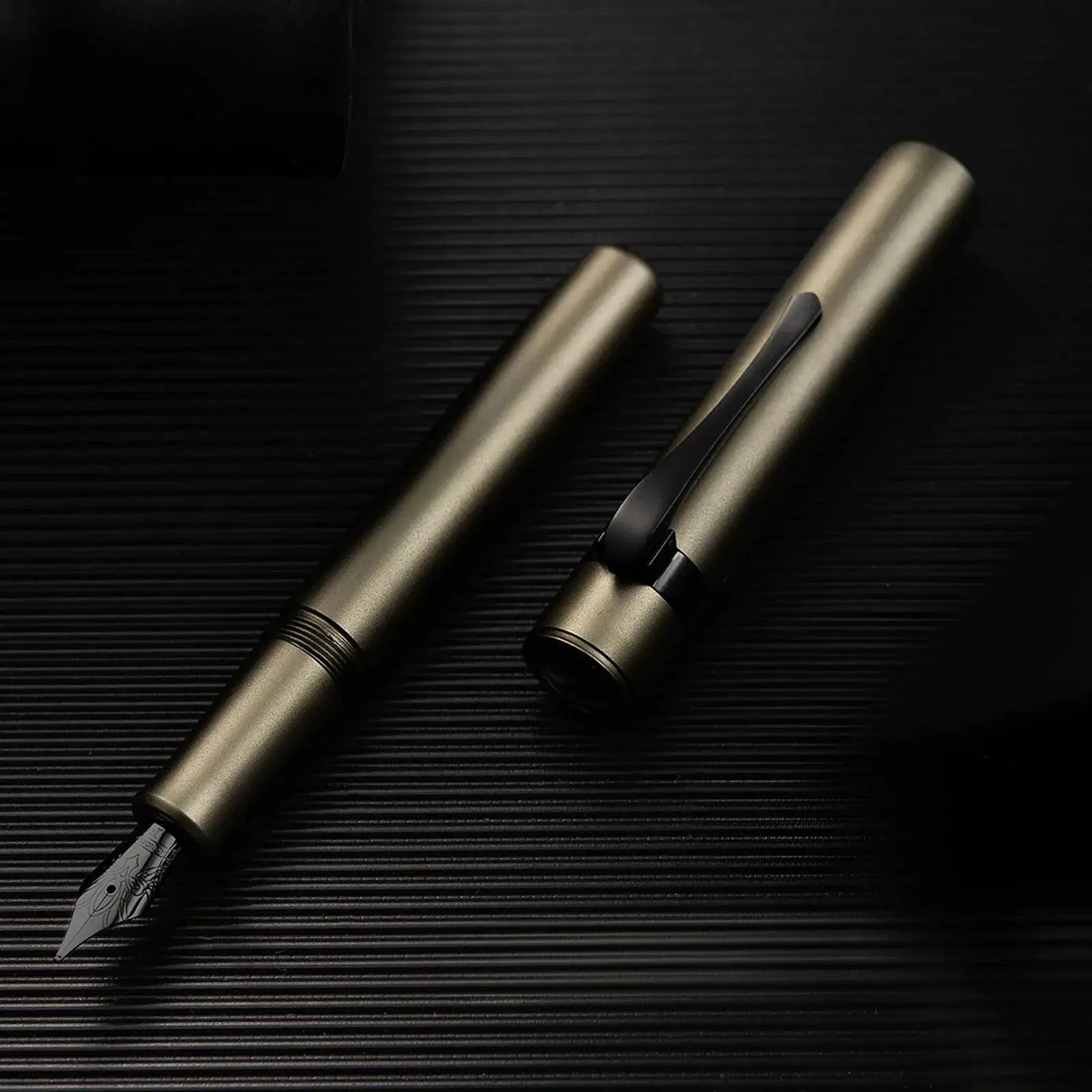 Hongdian M2 fountain pen set, two bronze-metal pens with black clips on a dark ribbed surface.