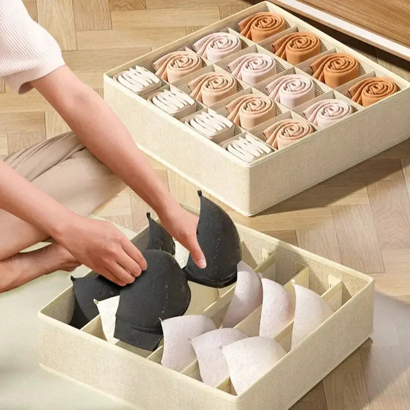 Two beige fabric underwear organizer boxes with dividers; one holds rolled socks, the other cup-shaped bra inserts