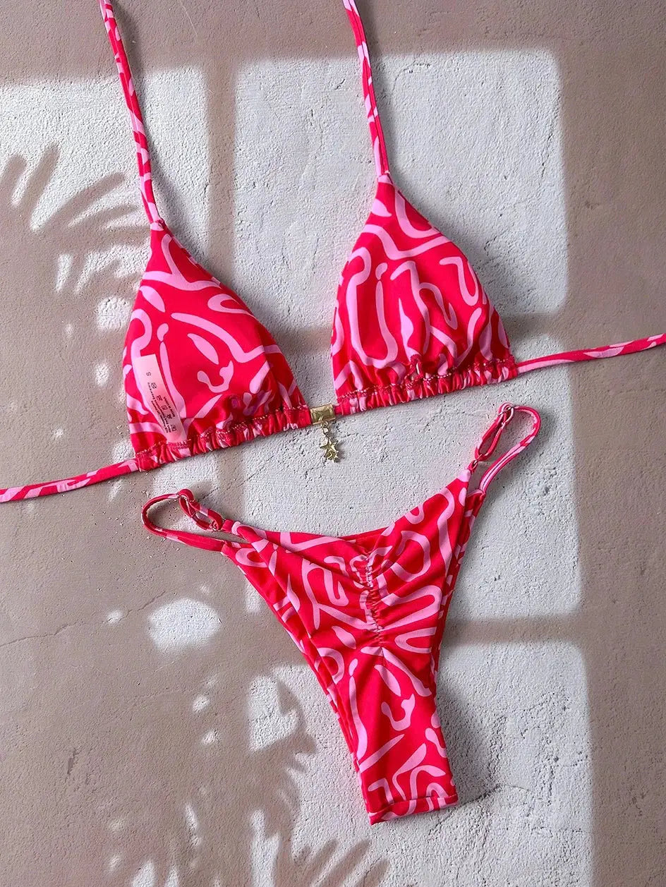 Simples Market pink two-piece bikini with white abstract print; triangle top with string ties, thong-style bottoms.