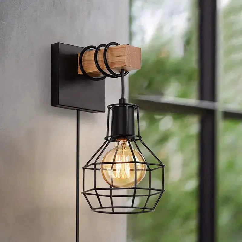 Wall sconce with black metal cage shade and wooden base bracket housing an Edison bulb