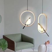 Pair of rotatable magpie bird LED pendant lights in gold and silver, hanging over a green sofa.