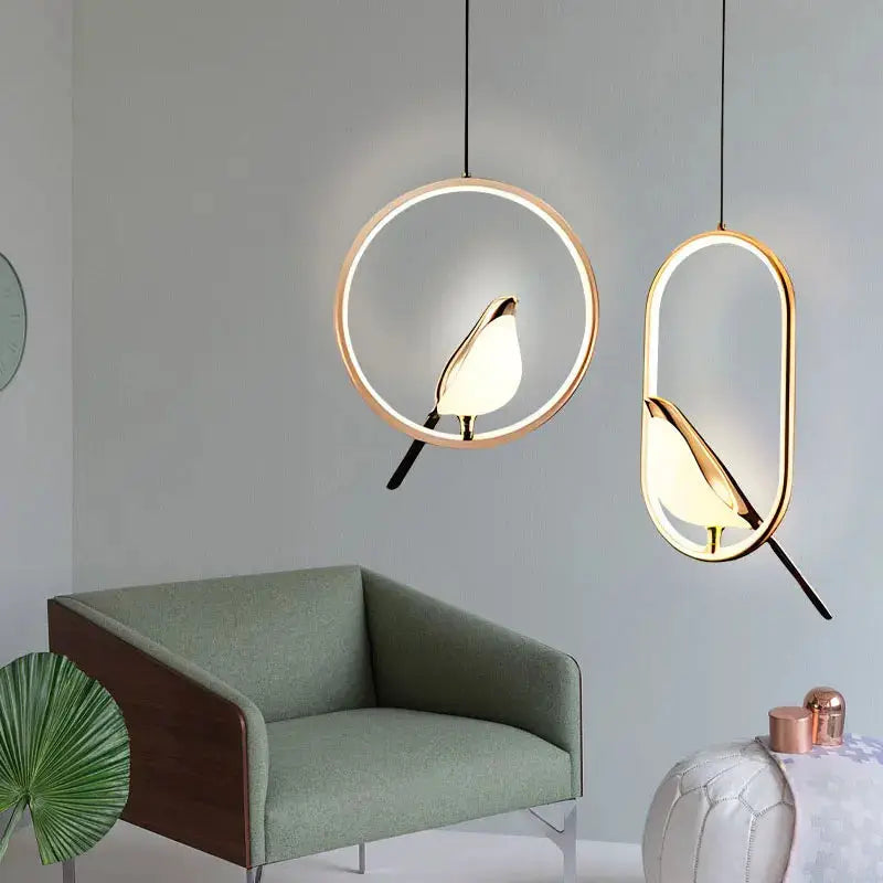 Pair of rotatable magpie bird LED pendant lights in gold and silver, hanging over a green sofa.