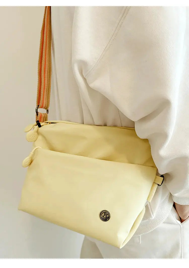 Simples Market ultra-light nylon crossbody bag in pale yellow with adjustable orange-striped strap and zipper closure