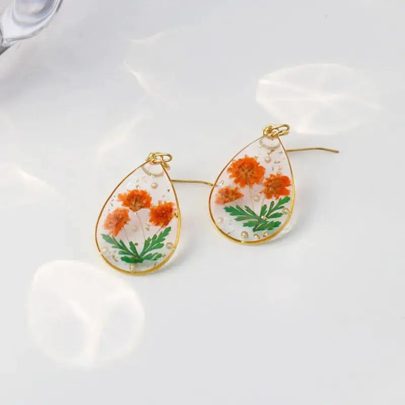 Teardrop pressed flower earrings in clear epoxy resin with orange blooms and green leaves, gold trim (set of 2)