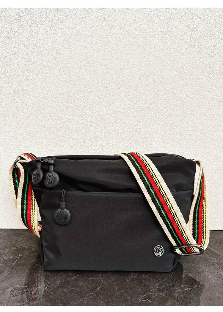 Crossbody bag by Simples Market, black nylon with wide striped adjustable strap, front zip pocket and zip closure.