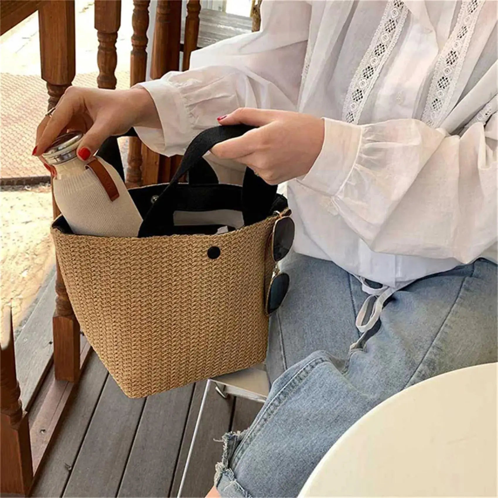 Elegant straw woven handbag; natural beige tote with top-handle carried by a person in a white lace blouse.