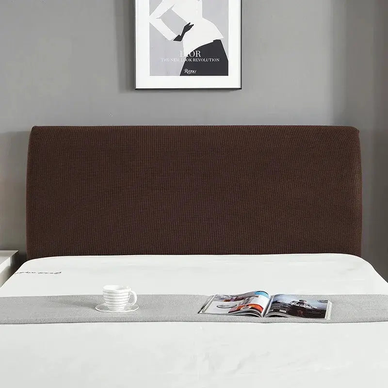 Brown elastic padded headboard cover on a bed with a gray runner, cup, and magazine