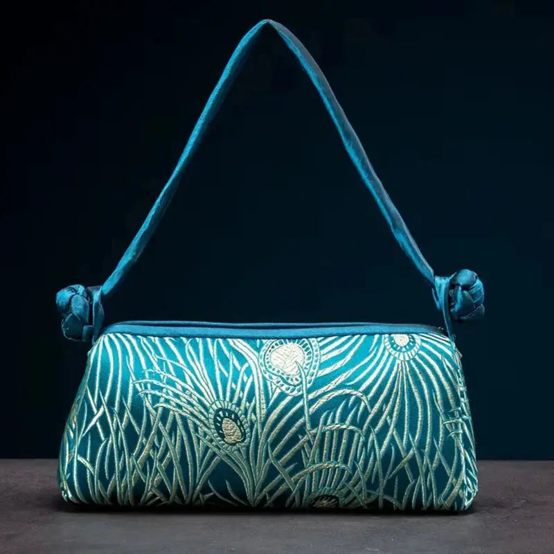 Teal satin shoulder bag with silver embroidered floral pattern and knotted strap.