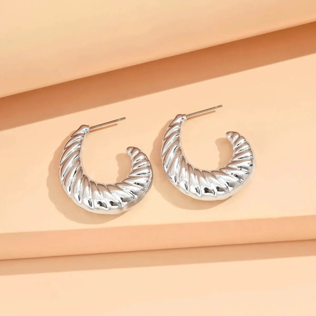 Geometric silver crescent hoop earrings with twisted ribbed texture; pair