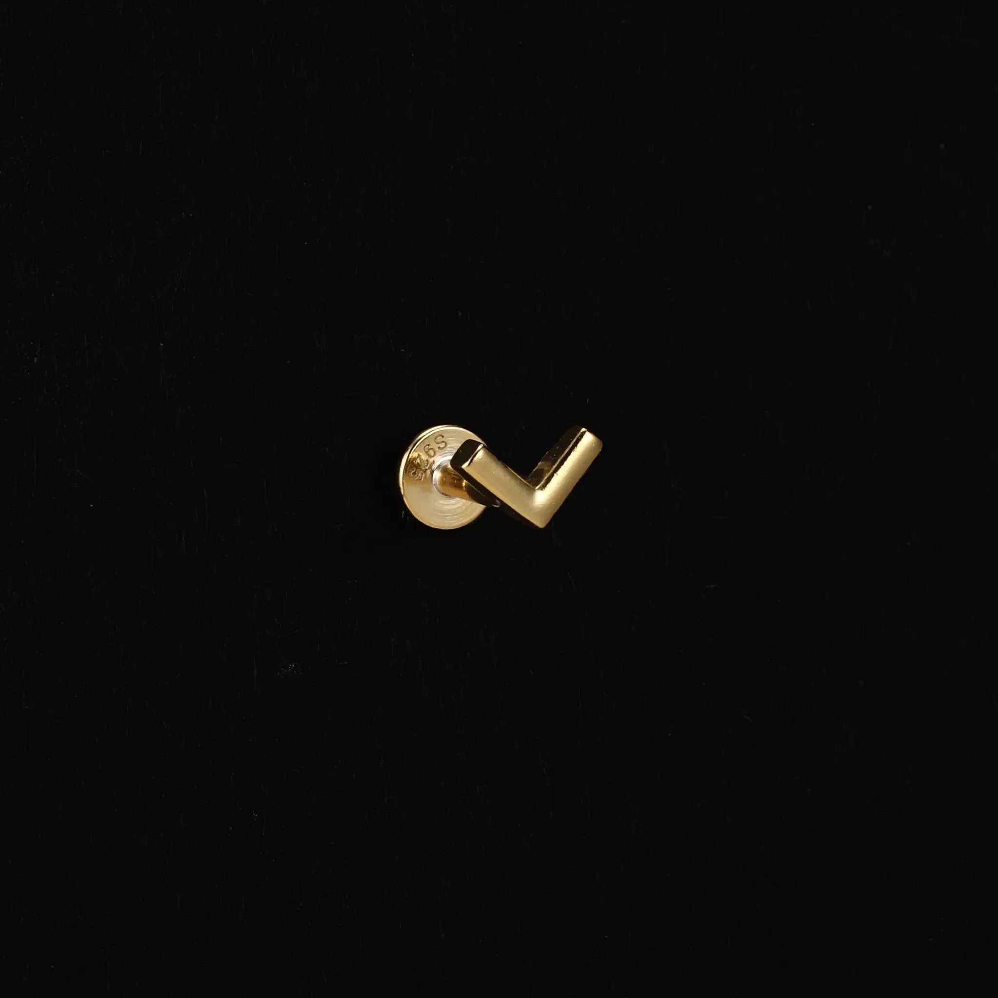 Gold-tone earring back and post of a Simples Market AIDE heart round ball flat-helix stud on black background.