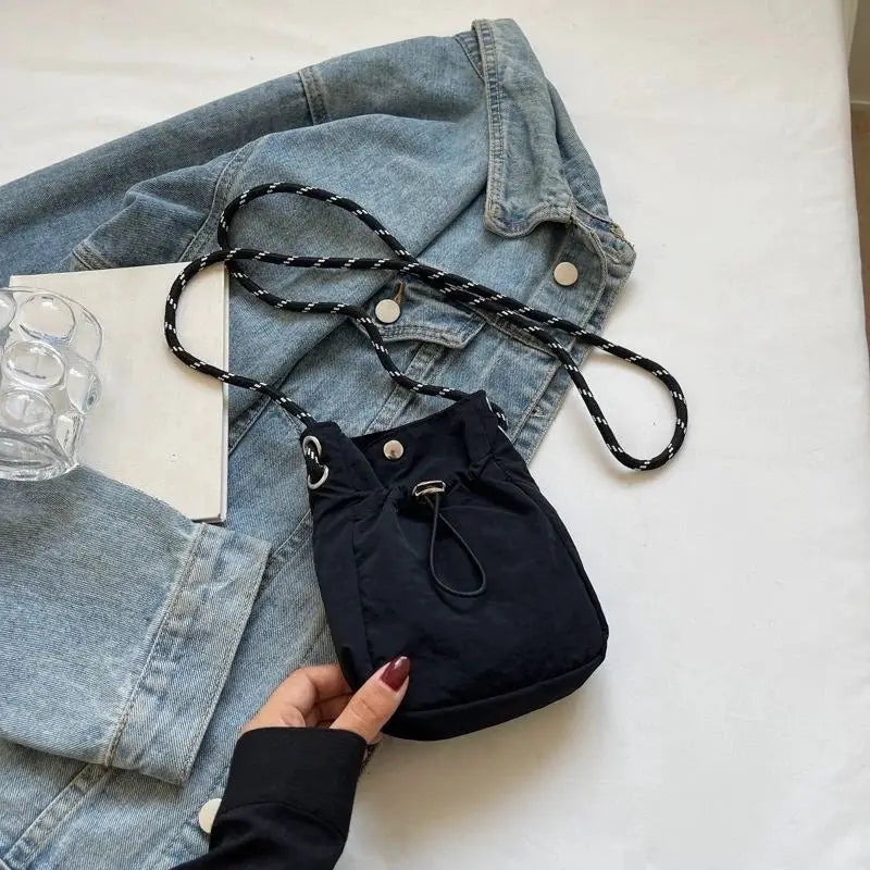 Nylon crossbody bag; small black mini purse with drawstring and braided black/white strap on denim jacket.