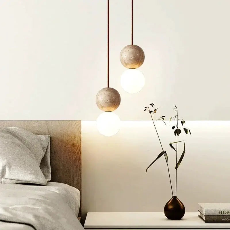 LED pendant lights with stone-cream wood beads and white globes, two hanging over a bedside table.