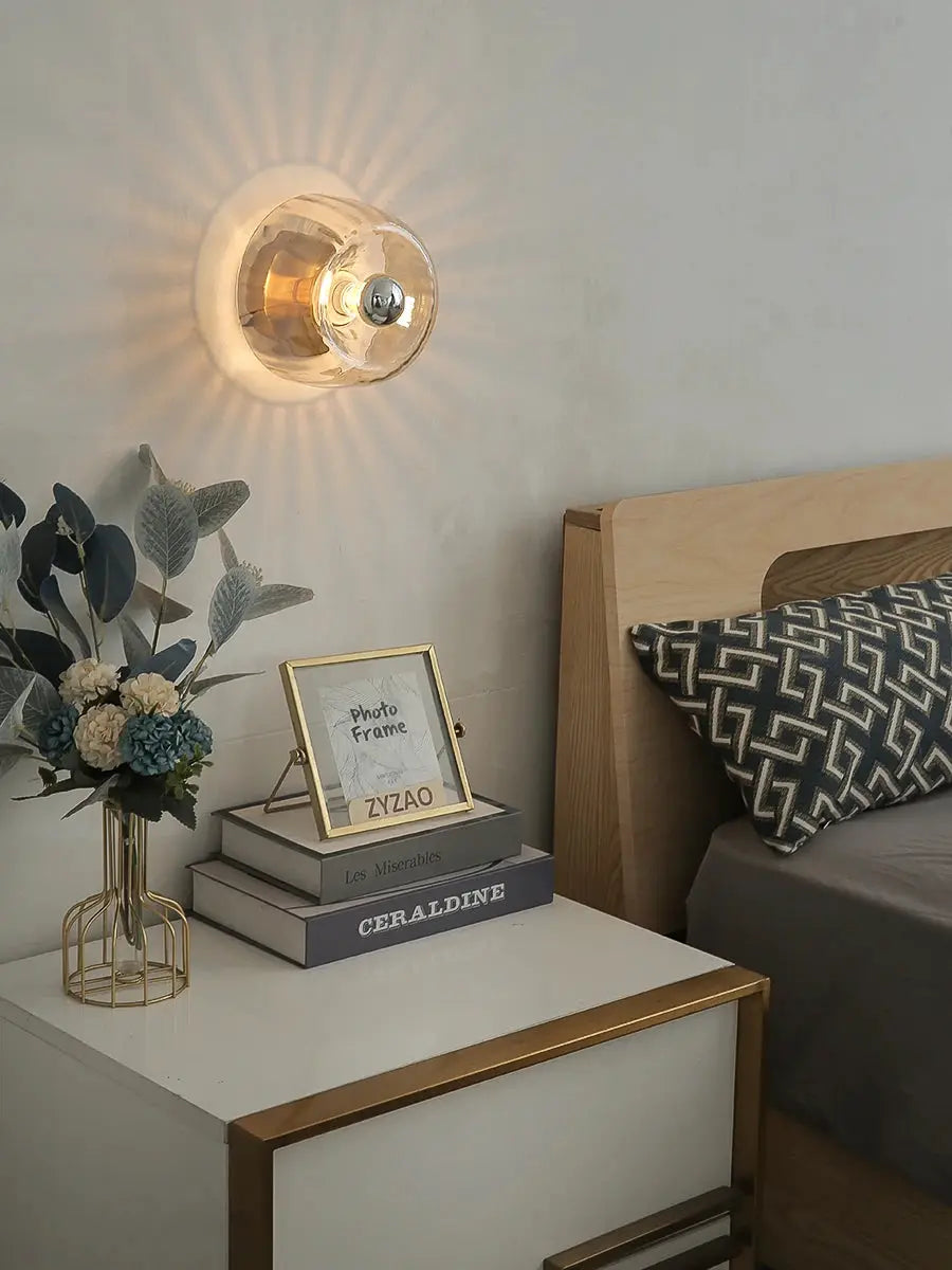LED Bauhaus glass wall lamp with a clear glass shade and brass finish, casting a warm glow on the wall.