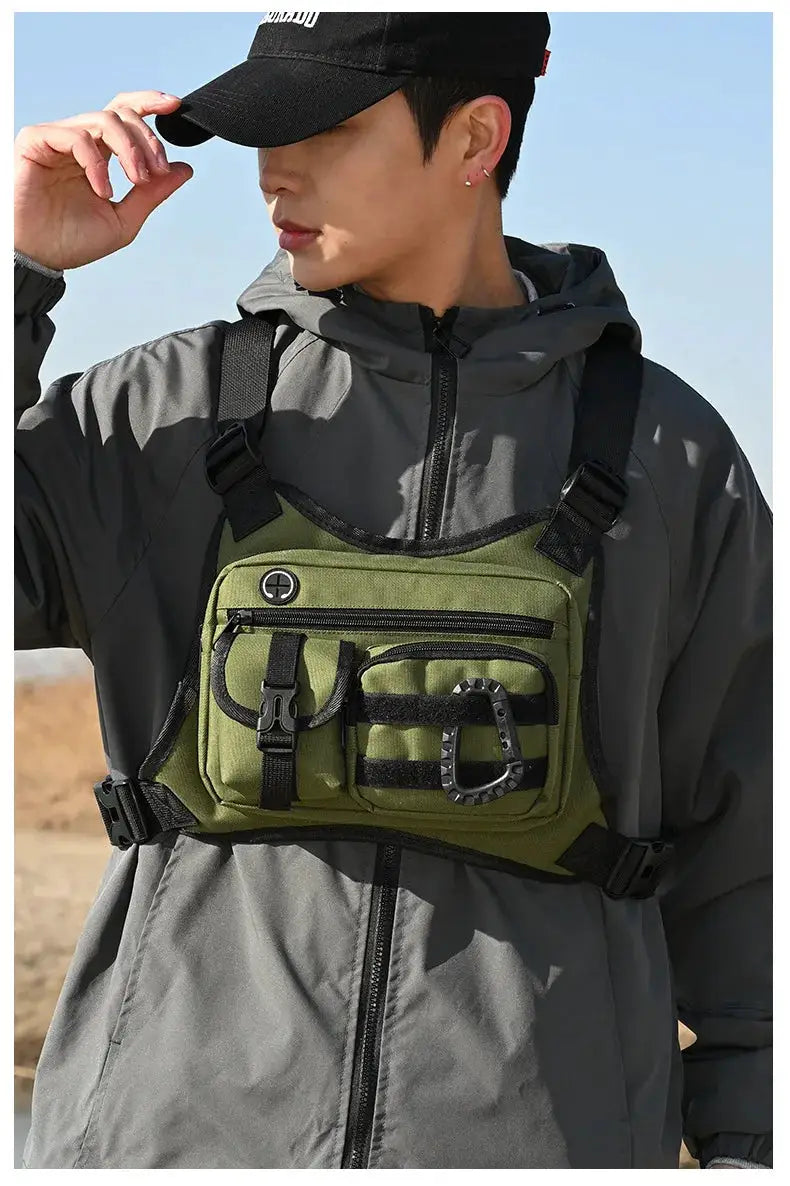 Outdoor tactical chest bag in olive green with black straps and multiple pockets worn over a gray jacket